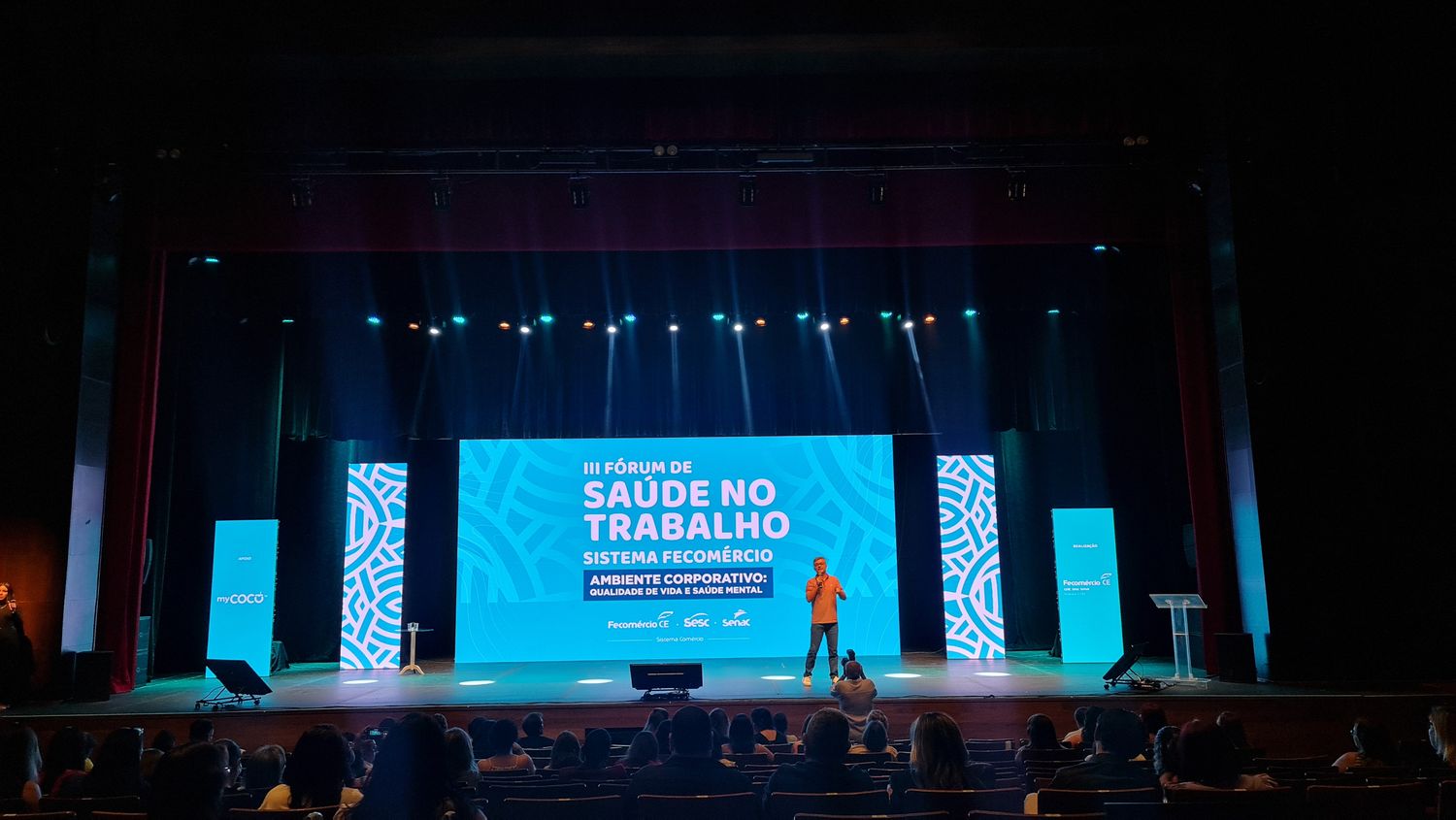 Plenária do Fórum de Saúde no Trabalho com painel de LED, totens de patrocínio e iluminação de teatro